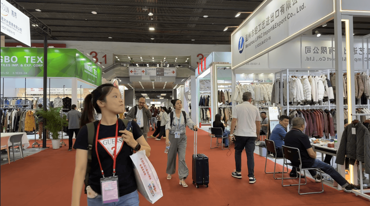 Visitors exploring the fashion and apparel section at Canton Fair 2025, browsing winter coats, textiles, and garments from global suppliers.