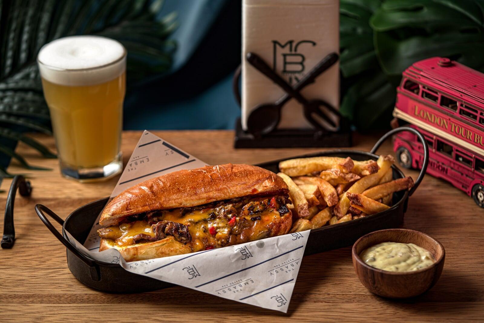 Juicy cheesesteak sandwich with melted cheese, crispy fries, and a cold craft beer at The Embassy Bar in Guangzhou.